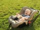 Babyschale auf dem Rasen mit lachendem Baby