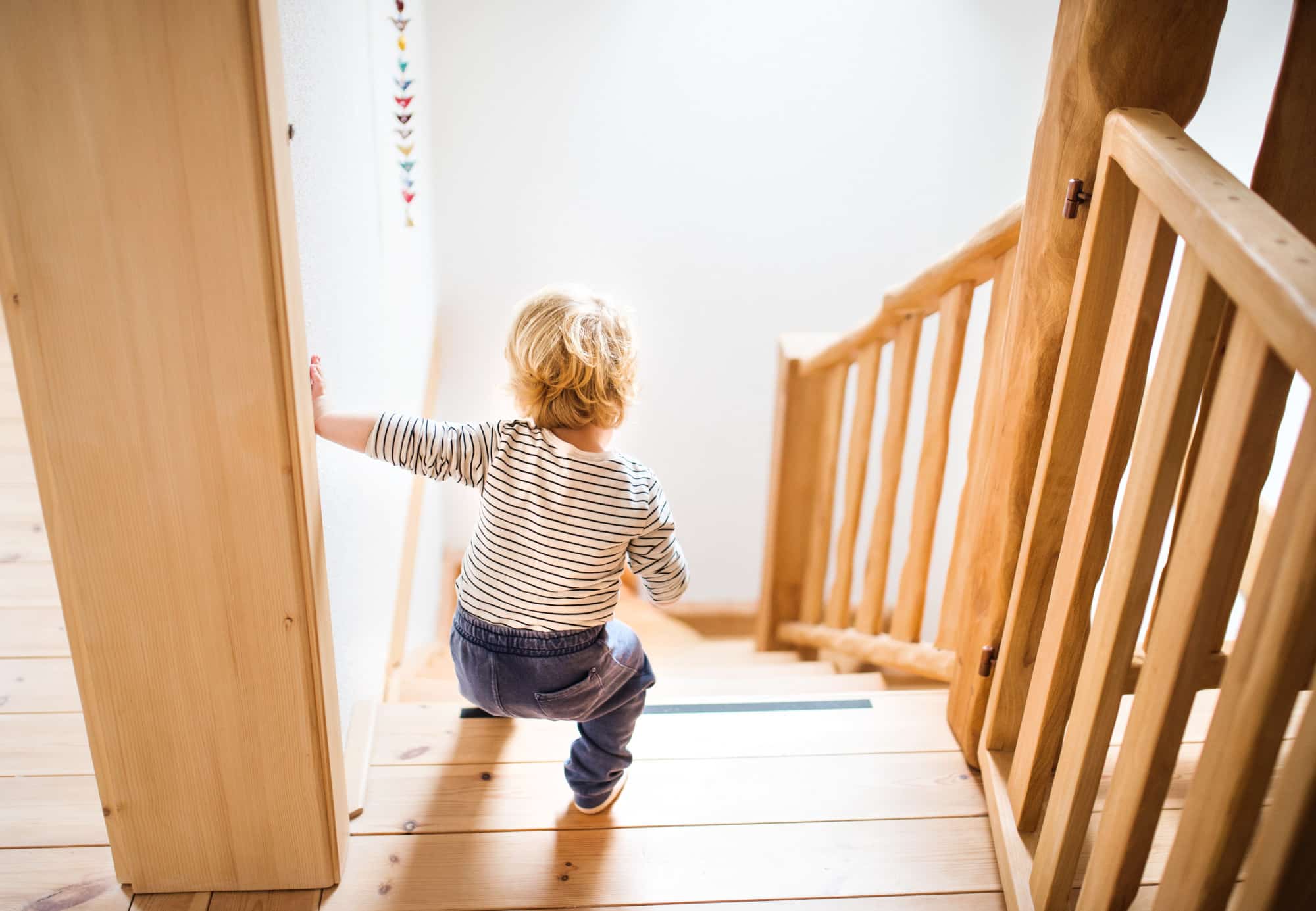 Ein Kleinkind geht unsicher allein eine steile Treppe hinab.