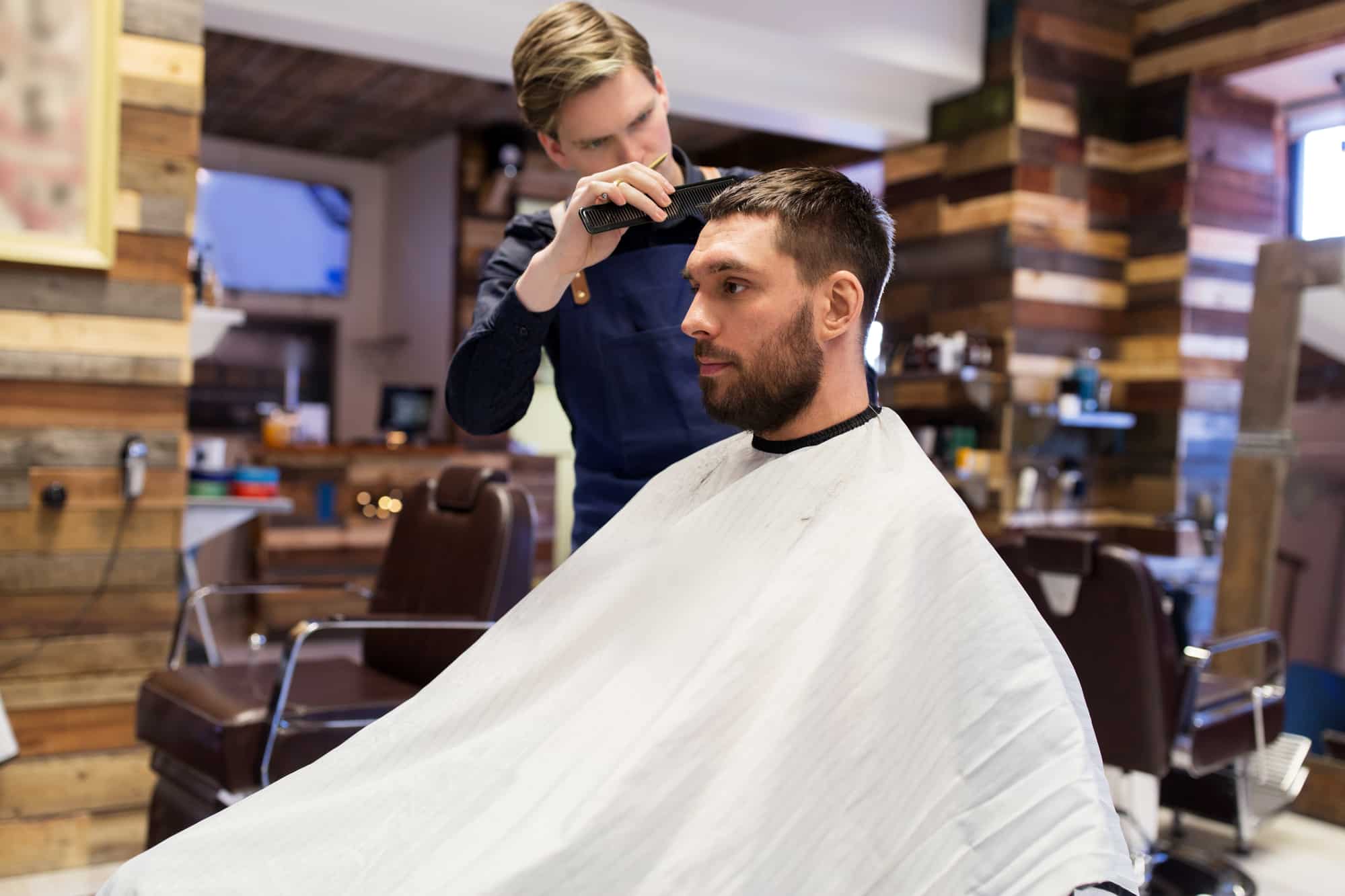 Friseur schneidet einem Mann mit weißem Umhang die Haare