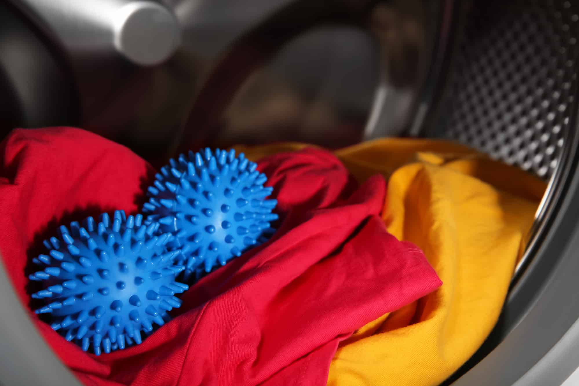 Zwei blaue Noppenbälle liegen auf roter und gelber Wäsche in einer Trommel