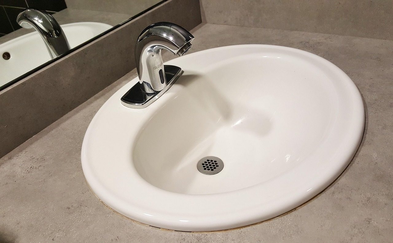 Weißes Waschbecken mit Ablauf und Wasserhahn in heller Arbeitsplatte