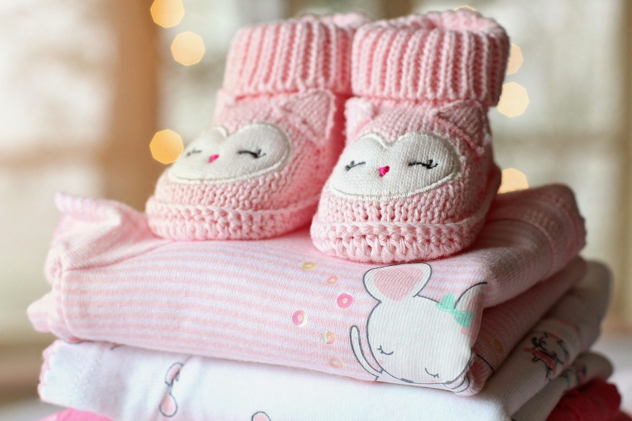 Rosa gestrickte Babyschuhe auf gefalteter Babykleidung