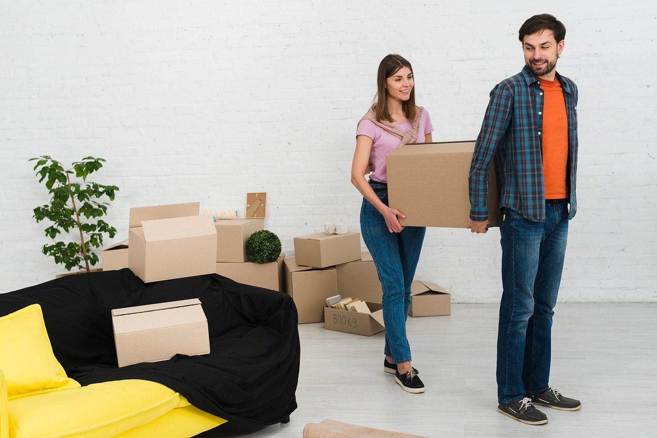 Paar trägt Umzugskartons durch eine fast leere Wohnung