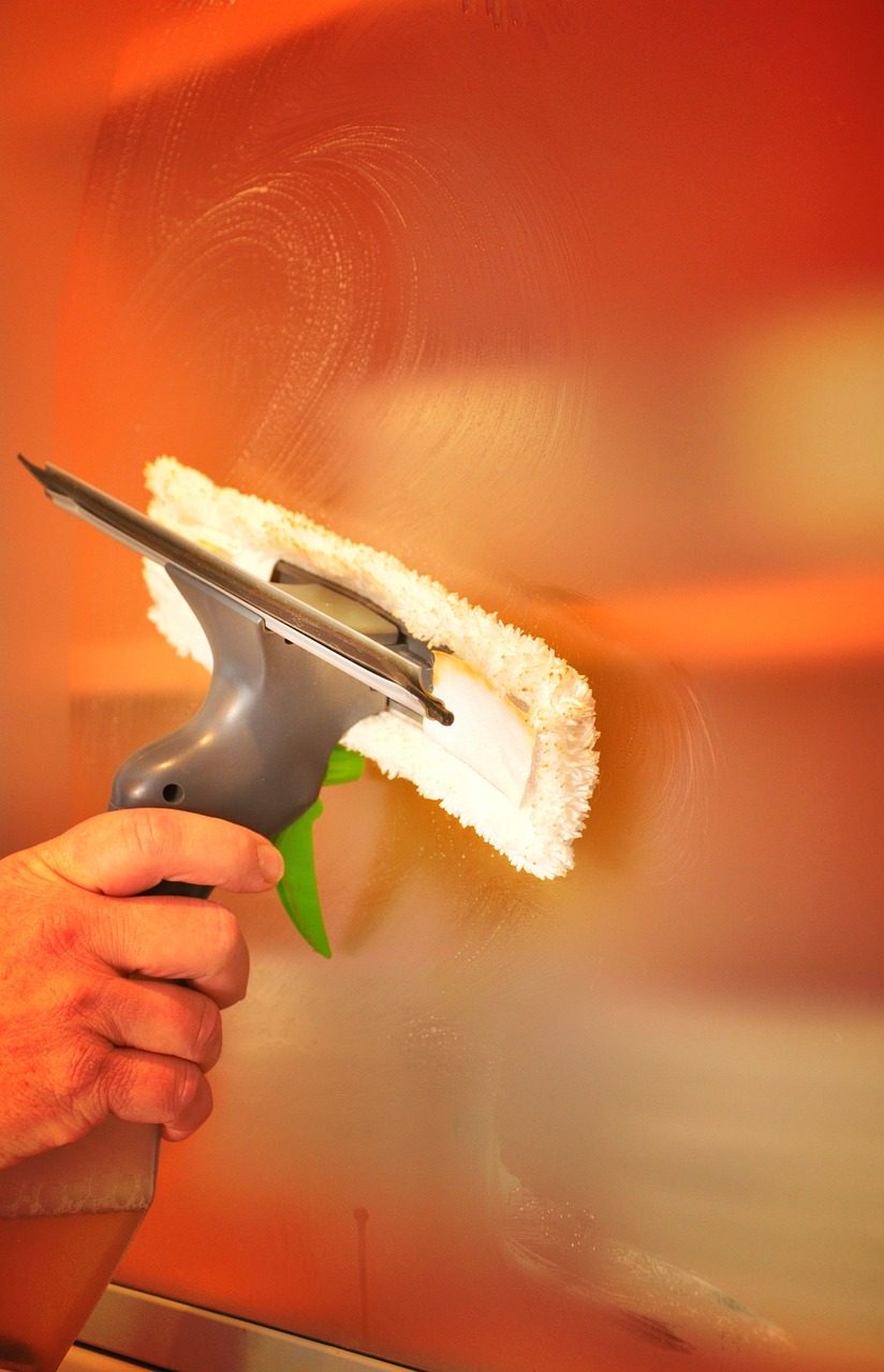 Hand führt einen Fensterwischer mit Einwascher über eine Glasscheibe