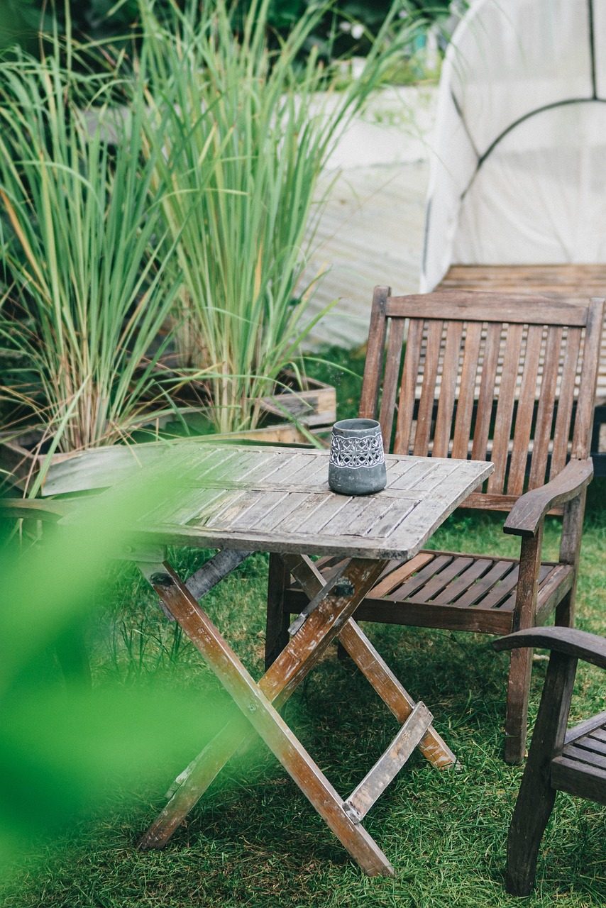 Vergrauter Holztisch mit Holzstühlen im Garten zwischen Gräsern