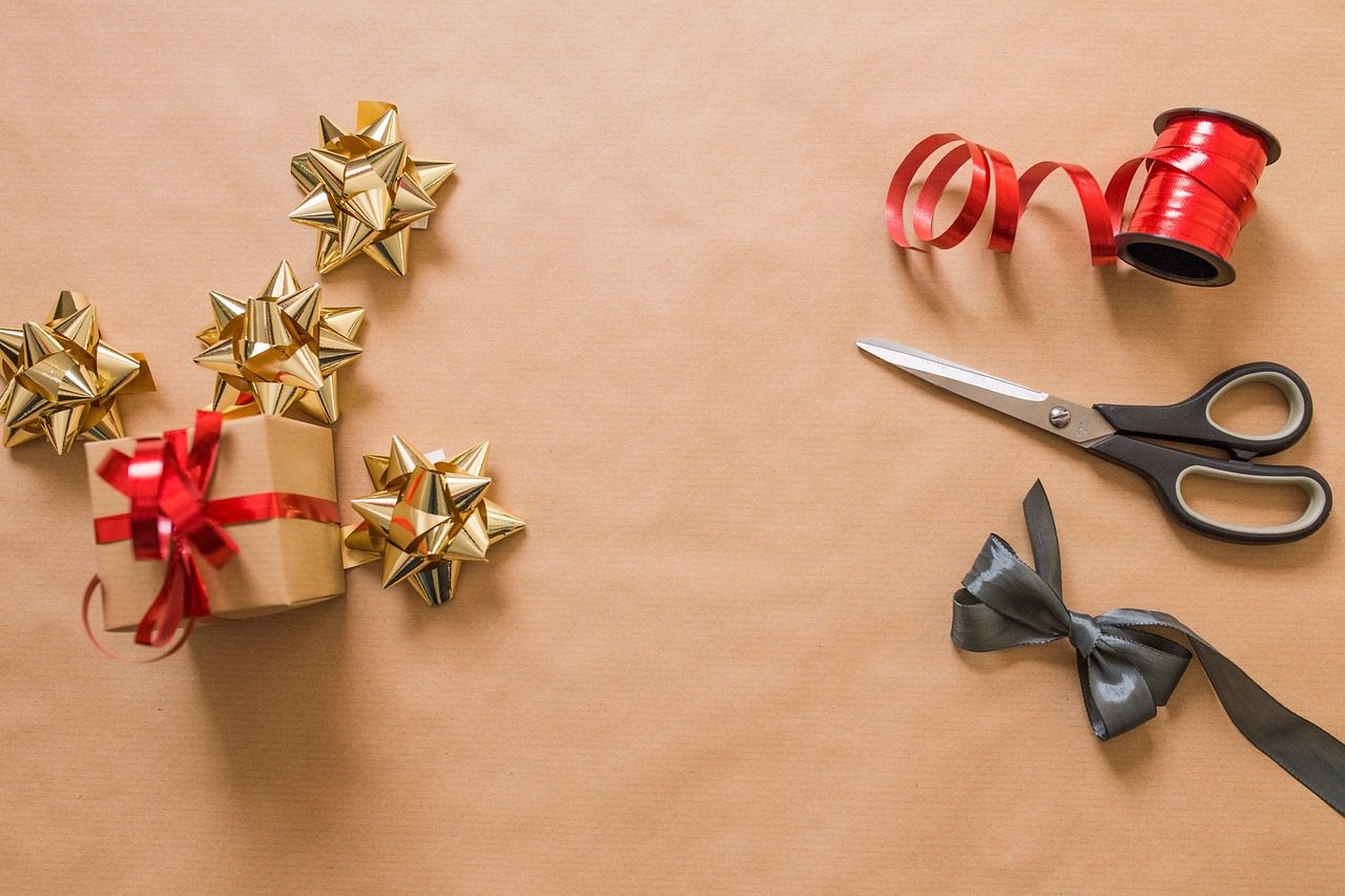 Kleine Geschenke, Schleifen, Band und Schere auf Packpapier