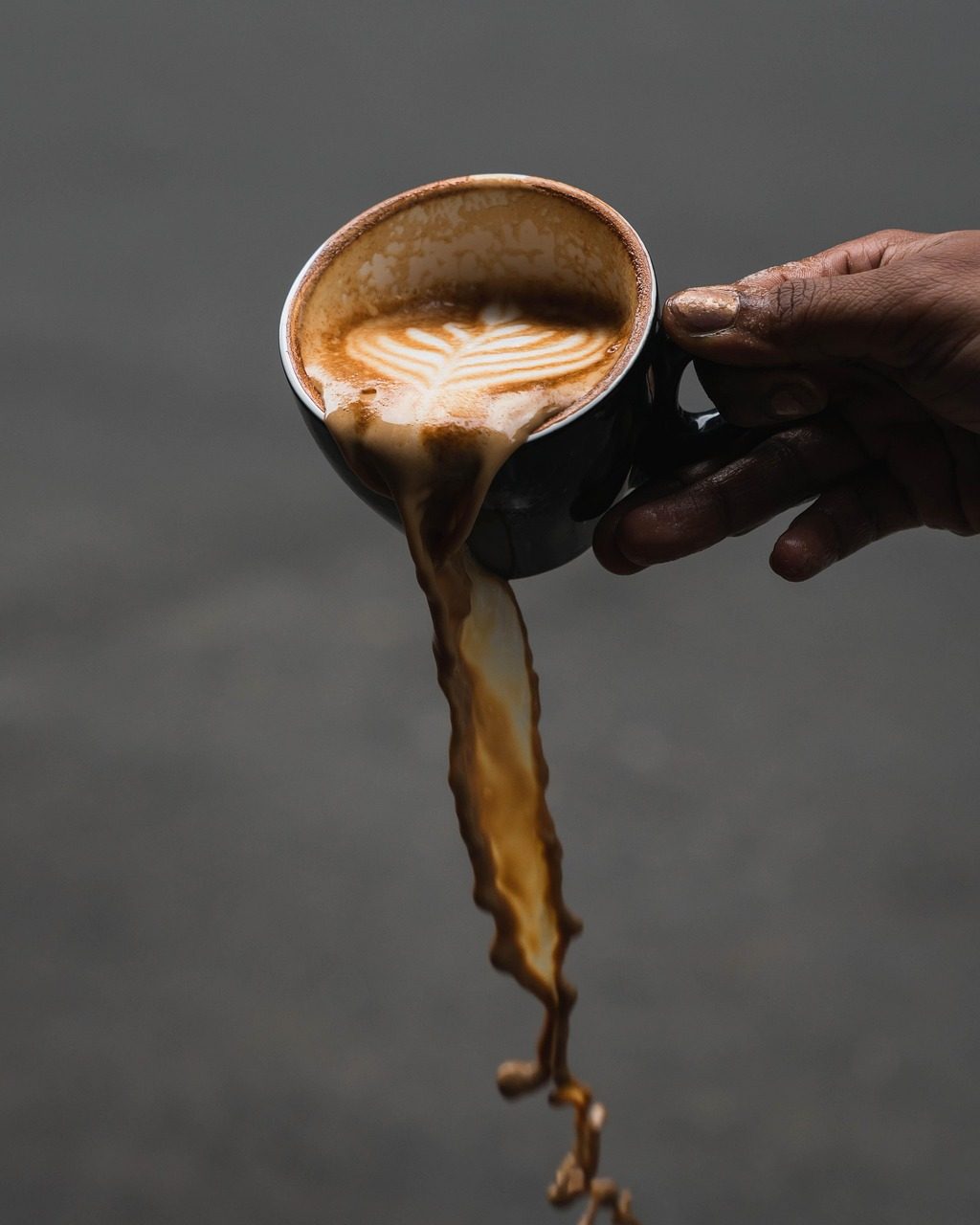 Hand kippt eine Tasse Milchkaffee aus, der Kaffee läuft heraus