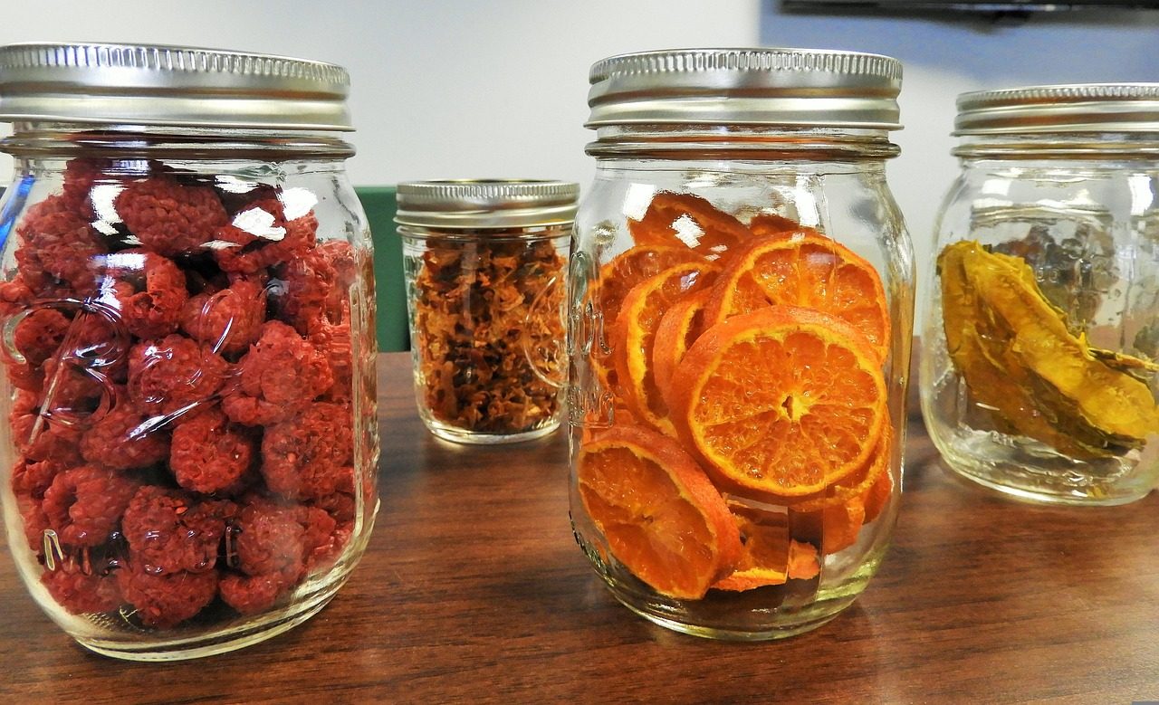 Gläser mit getrockneten Himbeeren, Orangenscheiben und Obst auf einem Tisch
