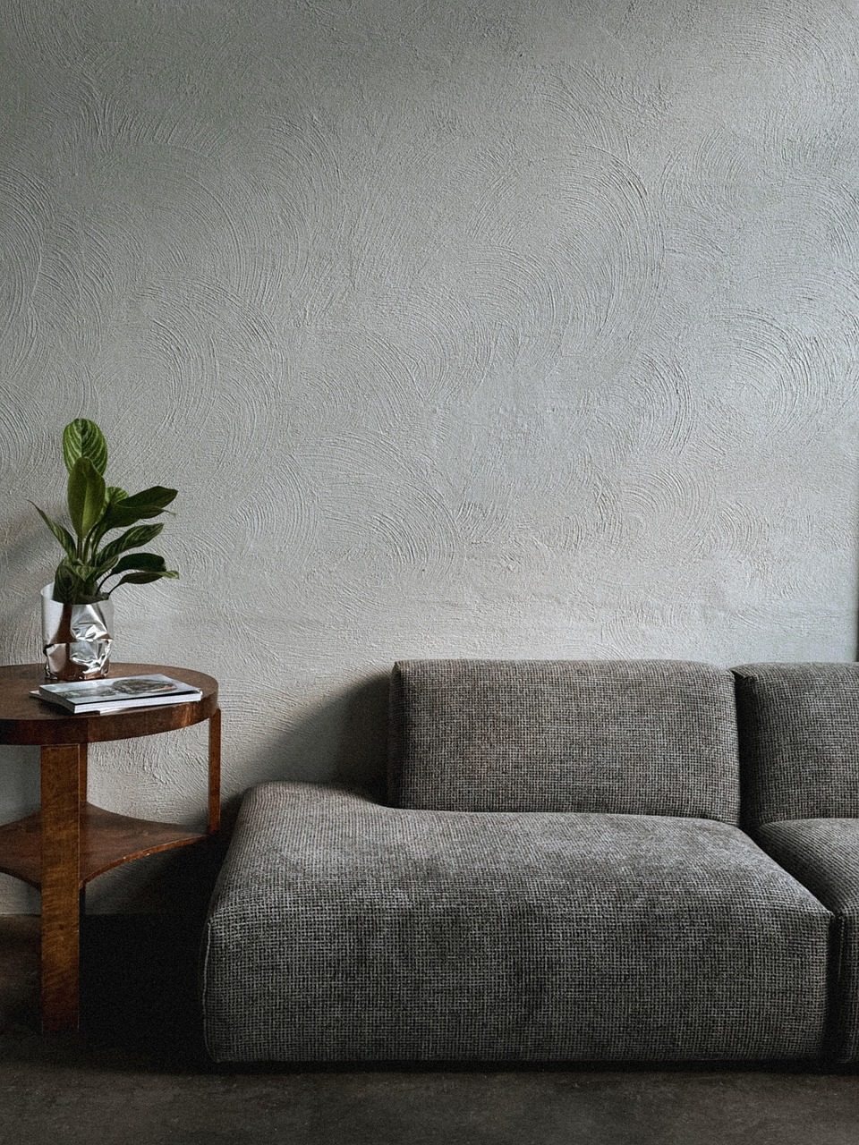 Graues Sofa und kleiner Beistelltisch vor einer hellgrauen Wand