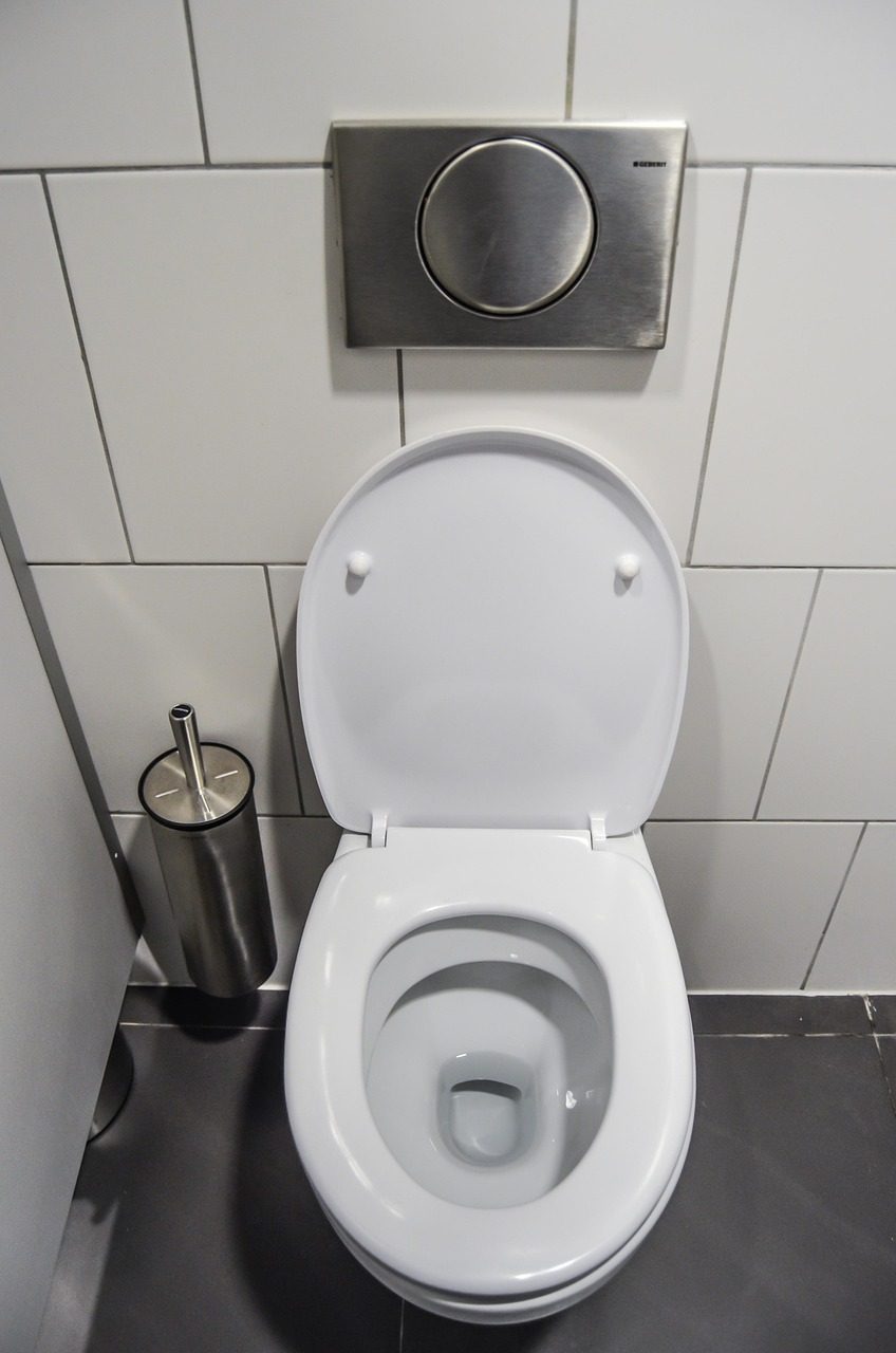 Weißes Wand-WC mit hochgeklapptem Deckel vor grauer Fliesenwand