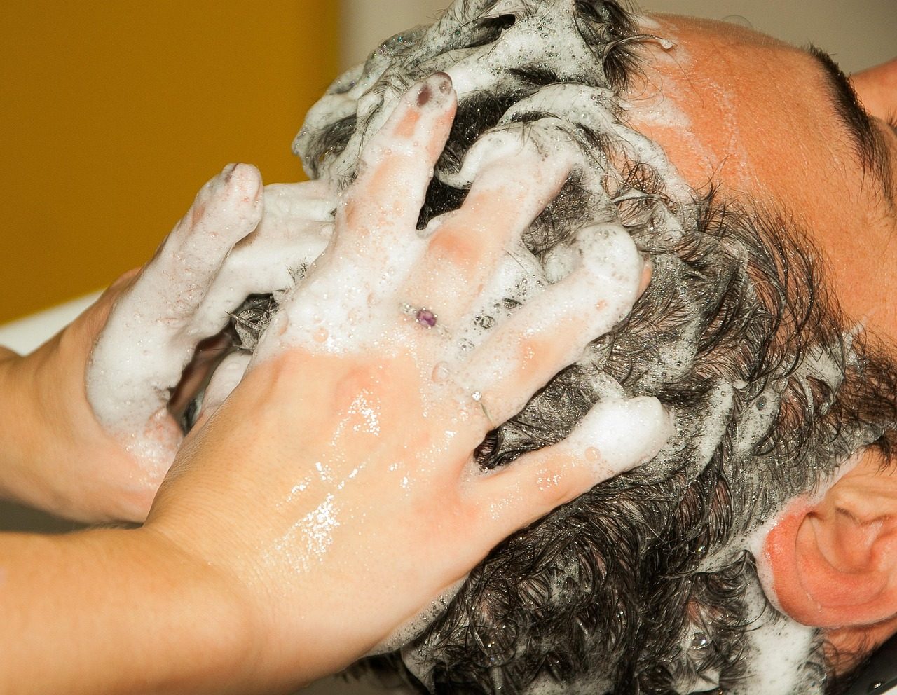 Hände massieren Shampooschaum in dunkles Haar ein